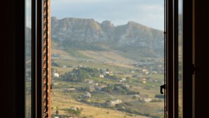 Janela aberta com vista para uma paisagem montanhosa e um vale abaixo.