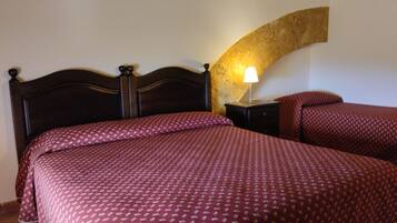A bedroom with a wooden headboard, a patterned bedspread, a nightstand with a lamp, and a curved wall.