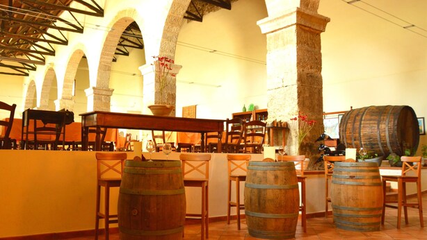 Um restaurante com mesas de madeira em estilo de barril, arcos de pedra e chão de azulejos.