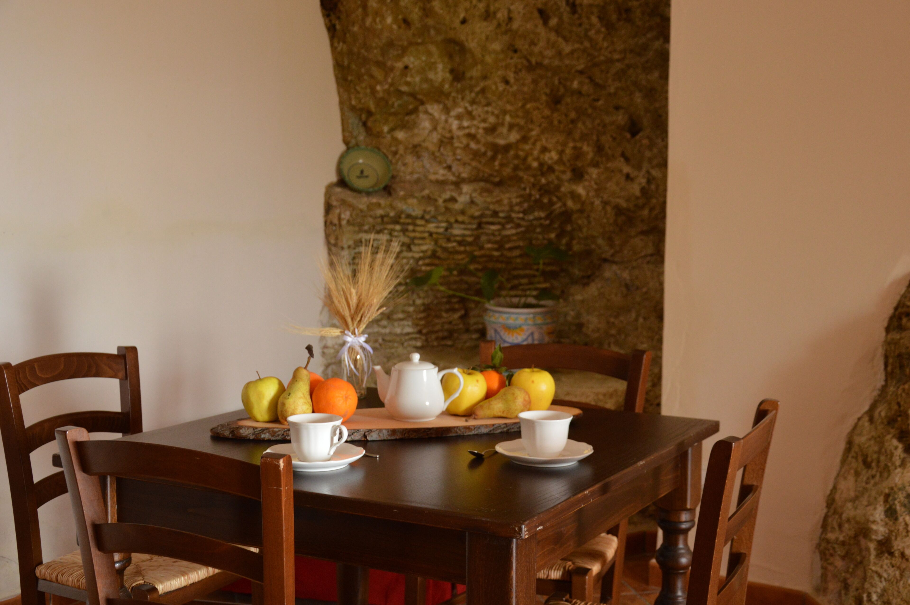 Una mesa de madera con sillas, un frutero, una tetera y tazas.
