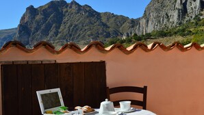 Mesa posta com louça branca e um laptop, com vista para uma paisagem montanhosa.