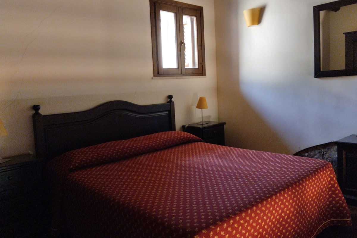 Ein Schlafzimmer mit Bett, Nachttisch, Lampe, Fenster und Spiegel.