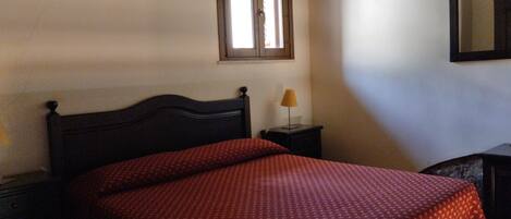 A bedroom with a bed, a nightstand, a lamp, a window, and a mirror.