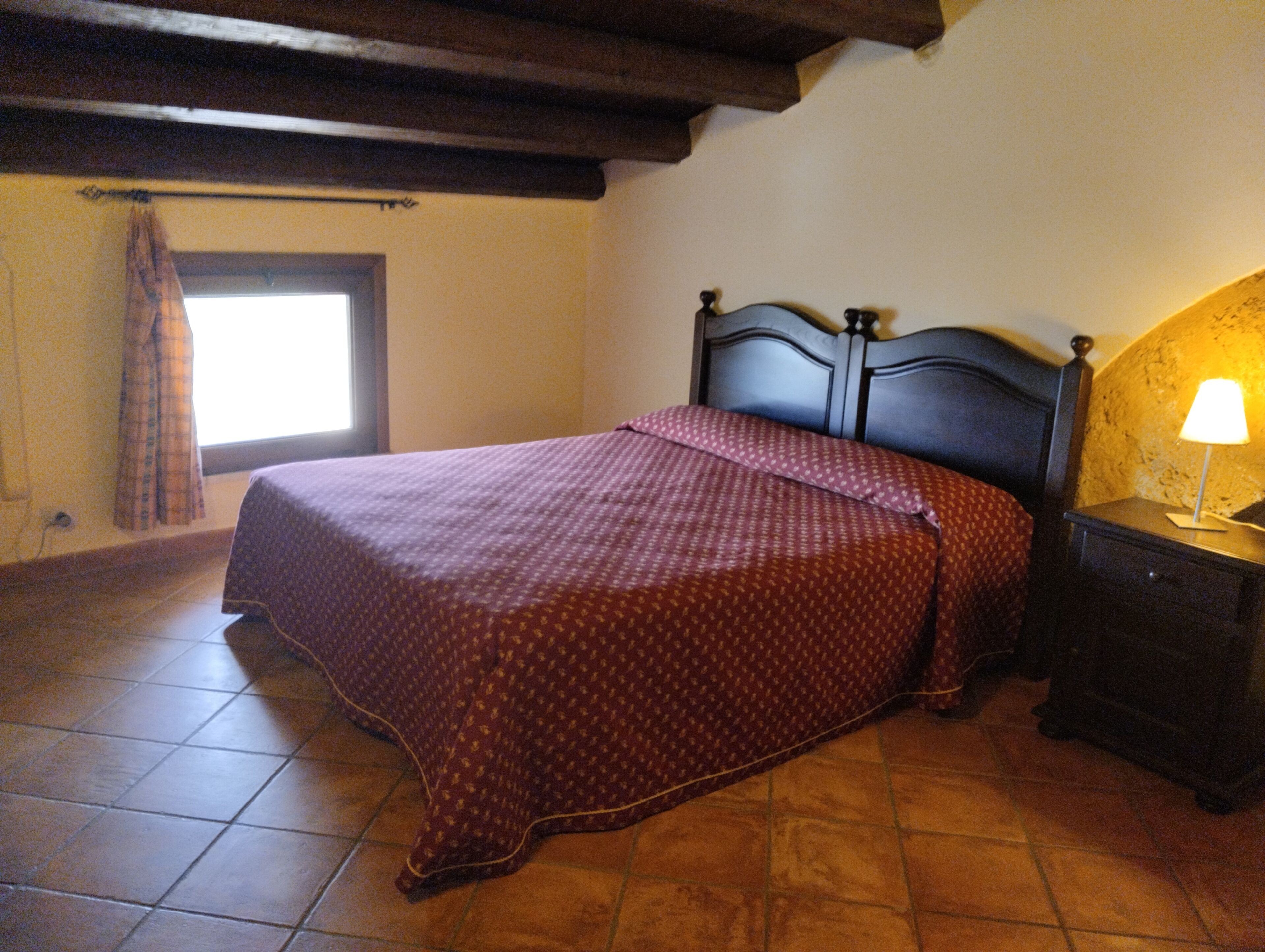 A bedroom with a bed, a nightstand, a window with curtains, and a lamp.
