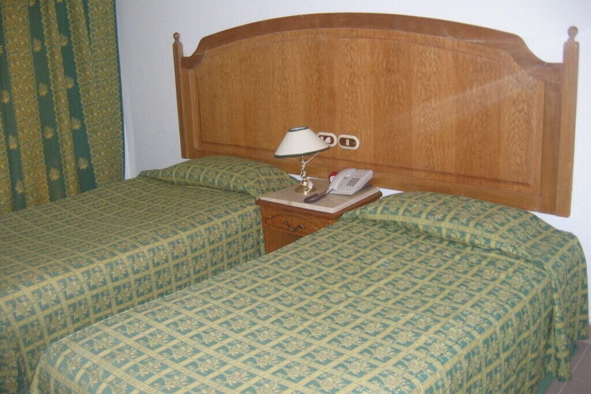 Un letto matrimoniale con testiera in legno, due comodini, una lampada e un telefono.