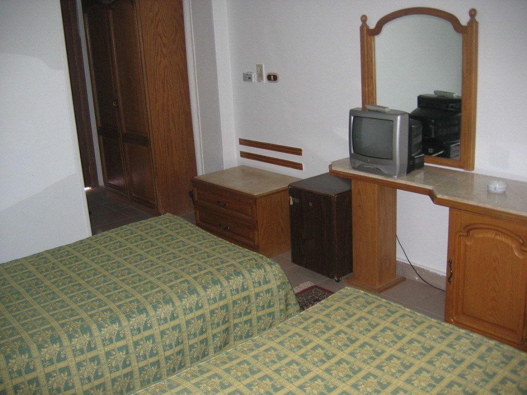 Una habitación con dos camas, un aparador de madera, un televisor y un espejo.