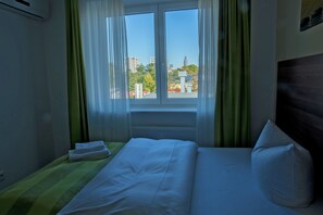 A hotel room with a bed, a window with curtains, and a view of buildings outside. - Goethe Conference Hotel by Trip Inn (Frankfurt)