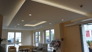 A modern interior with a high ceiling, recessed lighting, large windows, and a seating area with a table and chairs. - Goethe Conference Hotel by Trip Inn (Frankfurt)