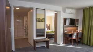 A hotel room with a shower, a bed, a desk with a chair, a TV, and a green curtain. - Goethe Conference Hotel by Trip Inn (Frankfurt)