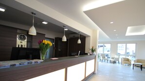 A modern reception area with a wooden reception desk, pendant lighting, and a clock on the wall. - Goethe Conference Hotel by Trip Inn (Frankfurt)