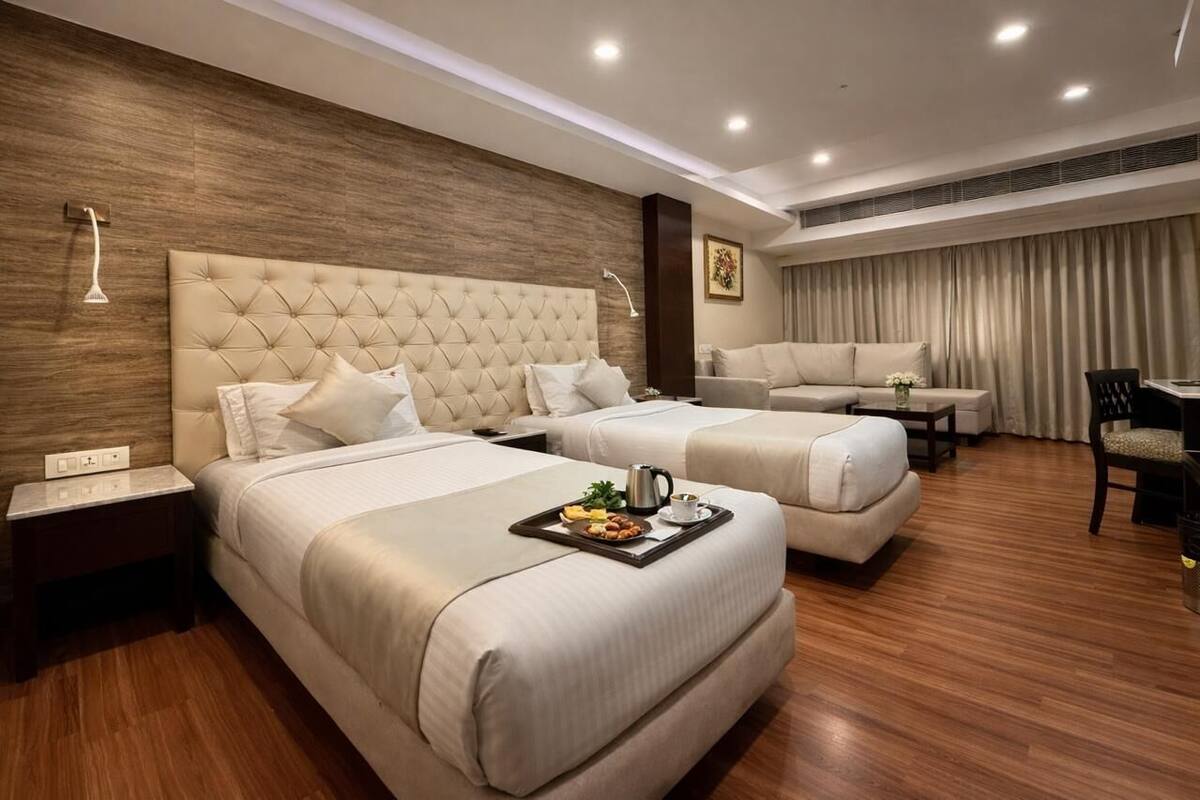 A hotel room with two beds, a sofa, a dining table, and a small kitchen area.