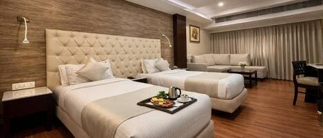 A hotel room with two beds, a sofa, a dining table, and a small kitchen area.