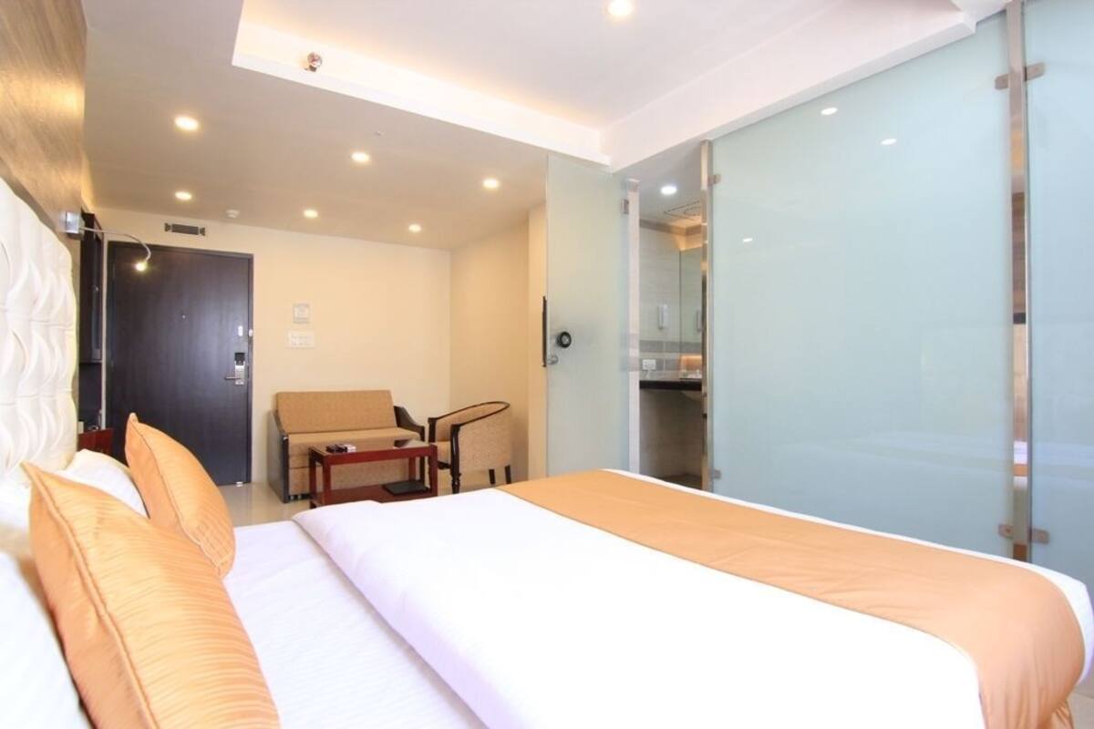 A hotel room with a bed, a chair, a desk, and a glass partition.