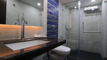 Un baño moderno con encimera de mármol, inodoro blanco, cabina de ducha de vidrio y pared con mosaico azul.