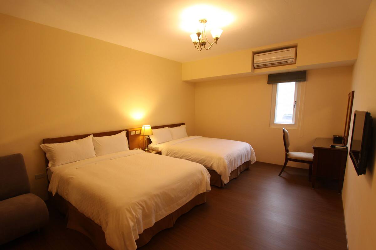 Habitación de hotel con dos camas, un escritorio, una silla, una lámpara y una ventana.