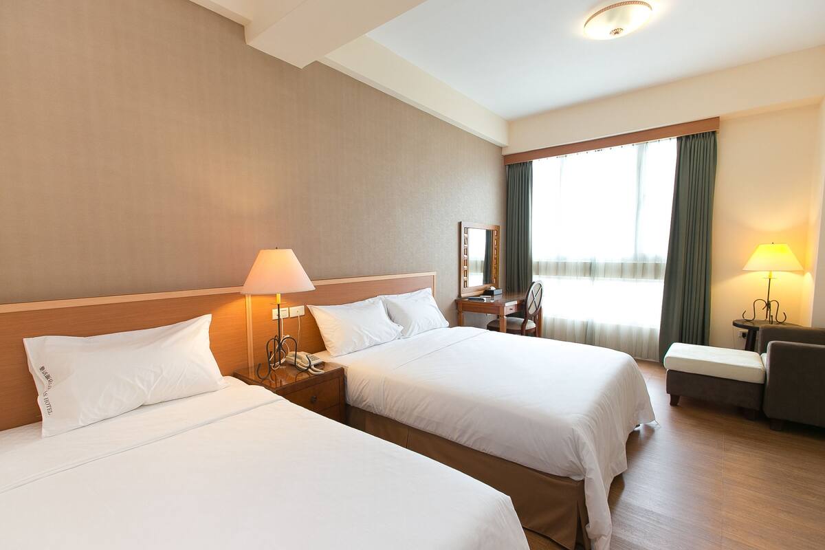 Habitación de hotel con dos camas, un escritorio, una silla y una ventana con cortinas.