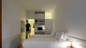 A modern bedroom with a large bed, a wooden floor, a built-in TV, and a small red table.