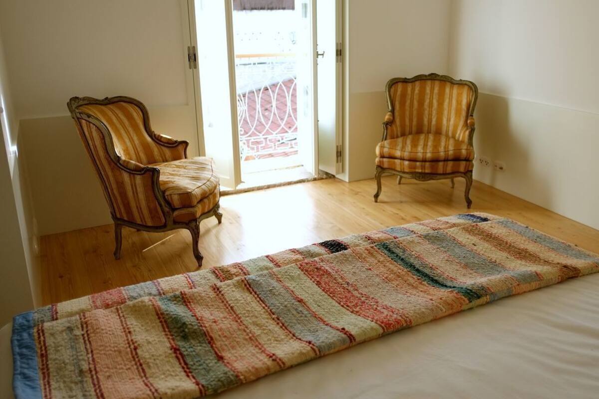 A room with a bed, two chairs, a patterned rug, and a door leading to an outdoor area.