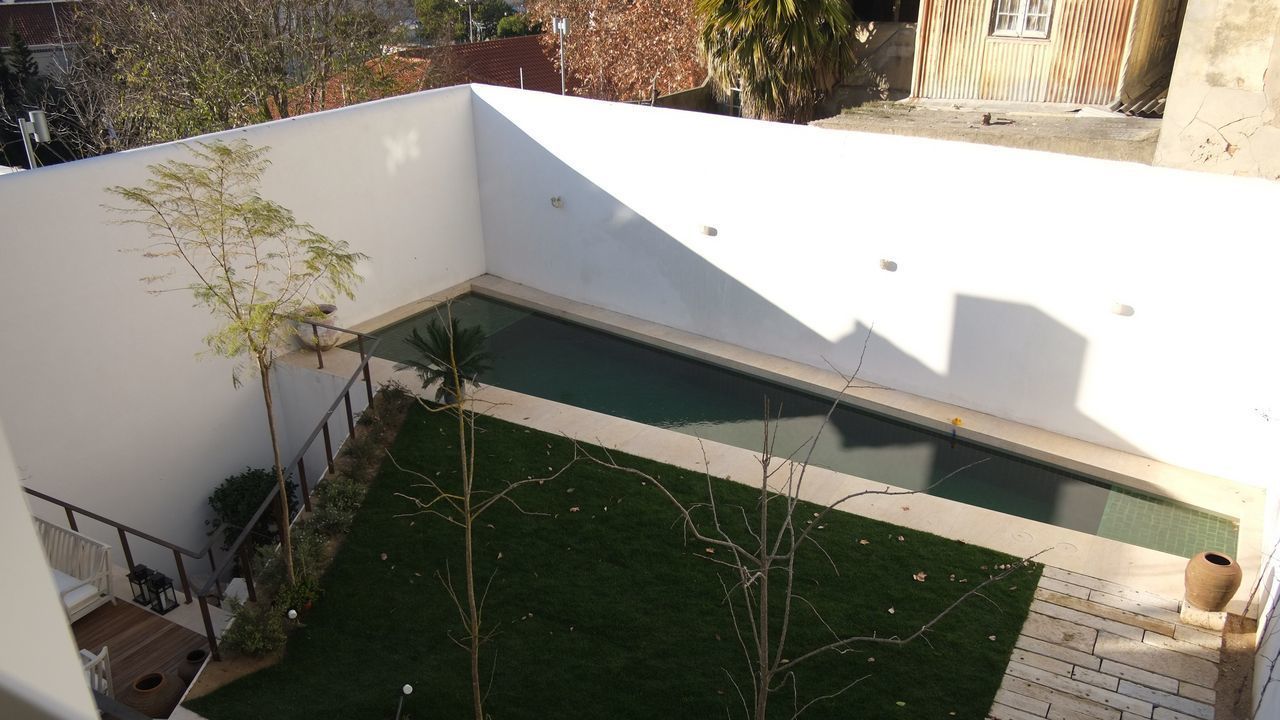 A rooftop pool with a small garden area, a staircase, and a white wall.
