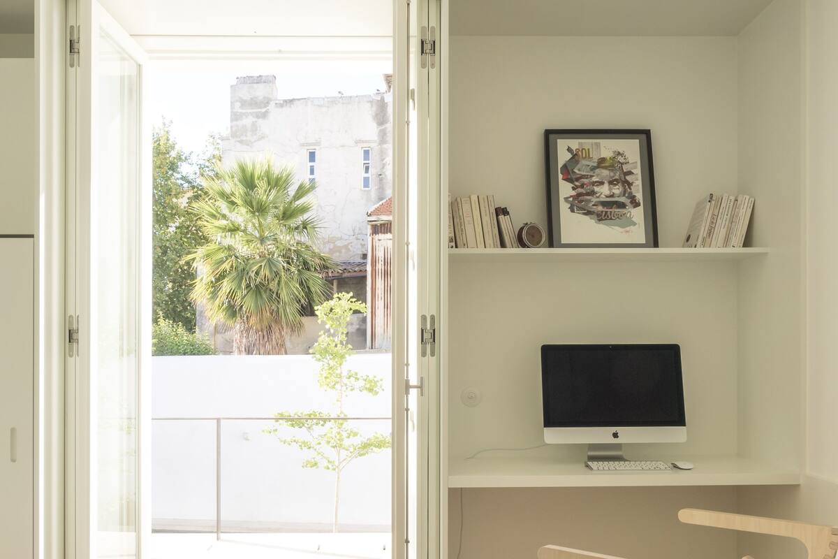 A modern bedroom with a bed, a desk with a computer, and a view of the outside.