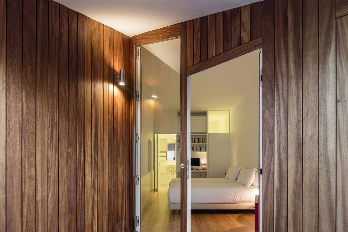 A room with wooden paneling, a bed, a desk, and a mirrored closet door.