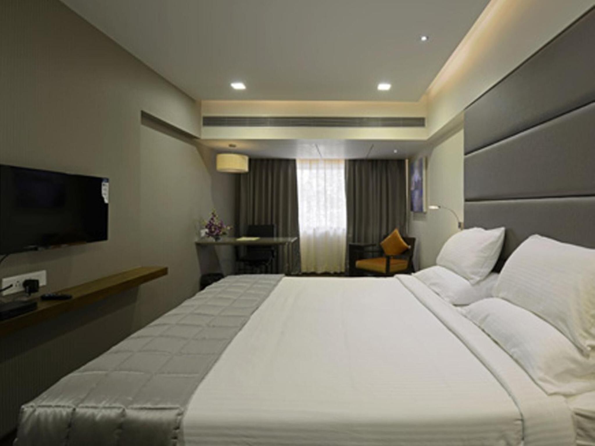 A hotel room with a large bed, a desk, a chair, a television, and a mirror.