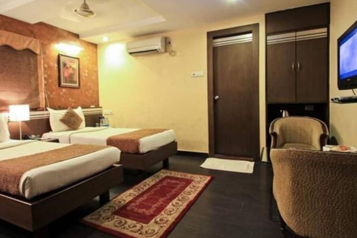 A hotel room with two beds, a desk, a chair, a television, and a wardrobe.