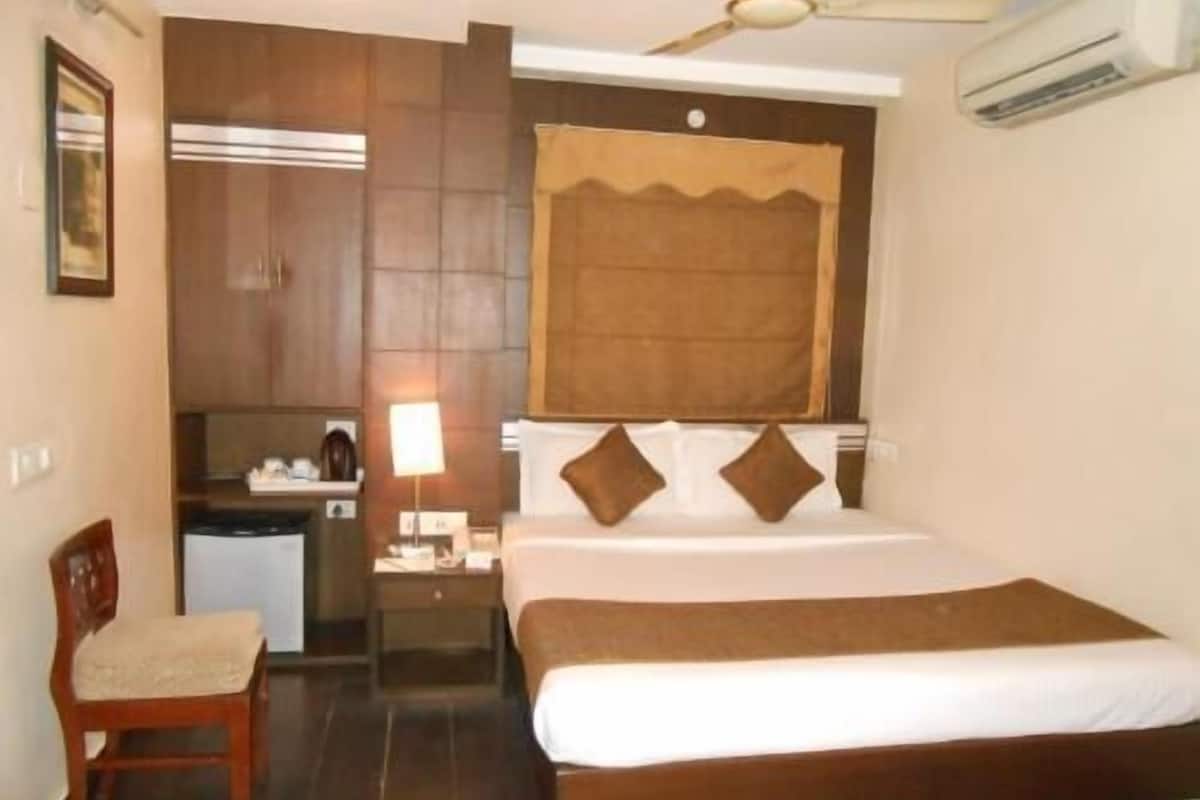 A hotel room with a bed, a chair, a desk, a lamp, and a ceiling fan.