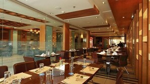 A spacious restaurant with multiple dining tables set for guests, large windows, and a modern interior design. - Hotel O2 VIP (Barasat)