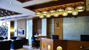 A hotel reception area with a modern design, featuring a wooden reception desk, a seating area with sofas, and a decorative ceiling light fixture. - Hotel O2 VIP (Barasat)