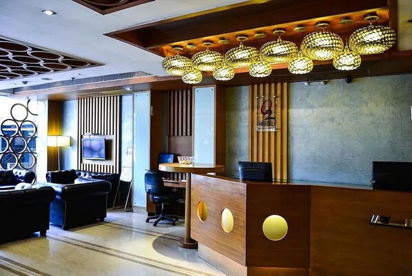 A hotel reception area with a modern design, featuring a wooden reception desk, a seating area with sofas, and a decorative ceiling light fixture. - Hotel O2 VIP (Barasat)