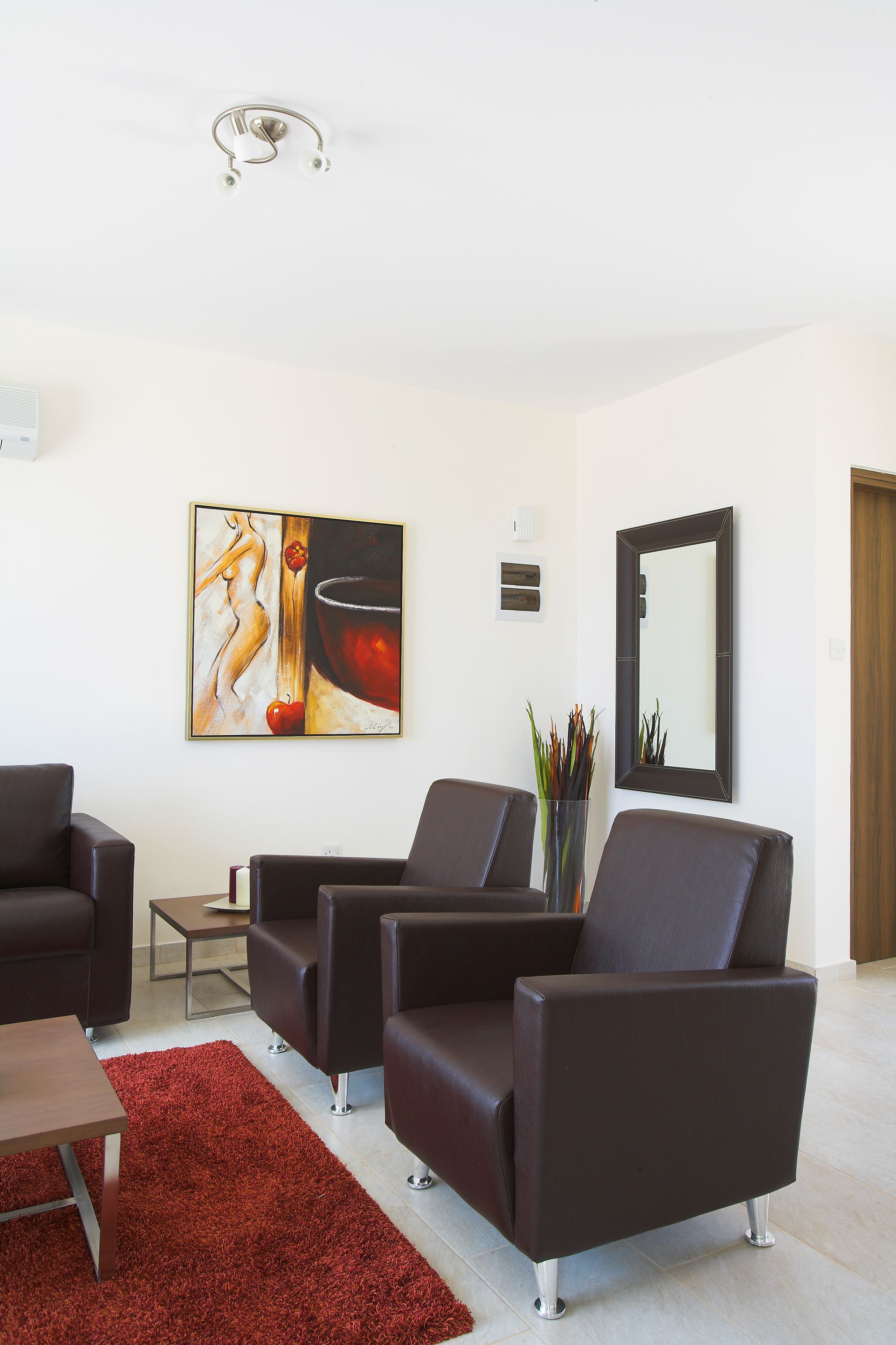 A modern living room with two black leather sofas, a red rug, a painting, and a mirror on the wall.