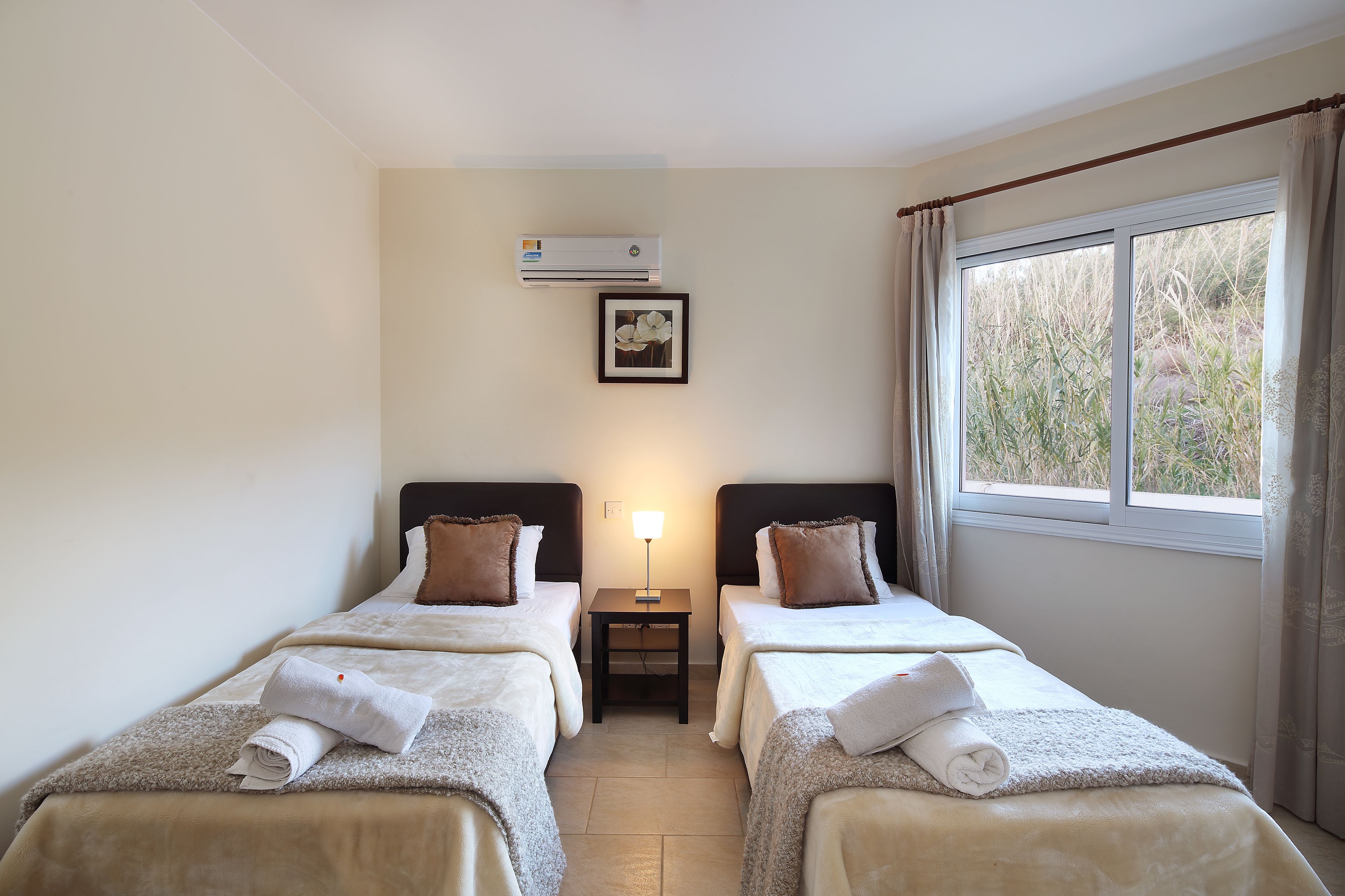 A hotel room with two beds, a nightstand, a lamp, an air conditioner, and a window with curtains.