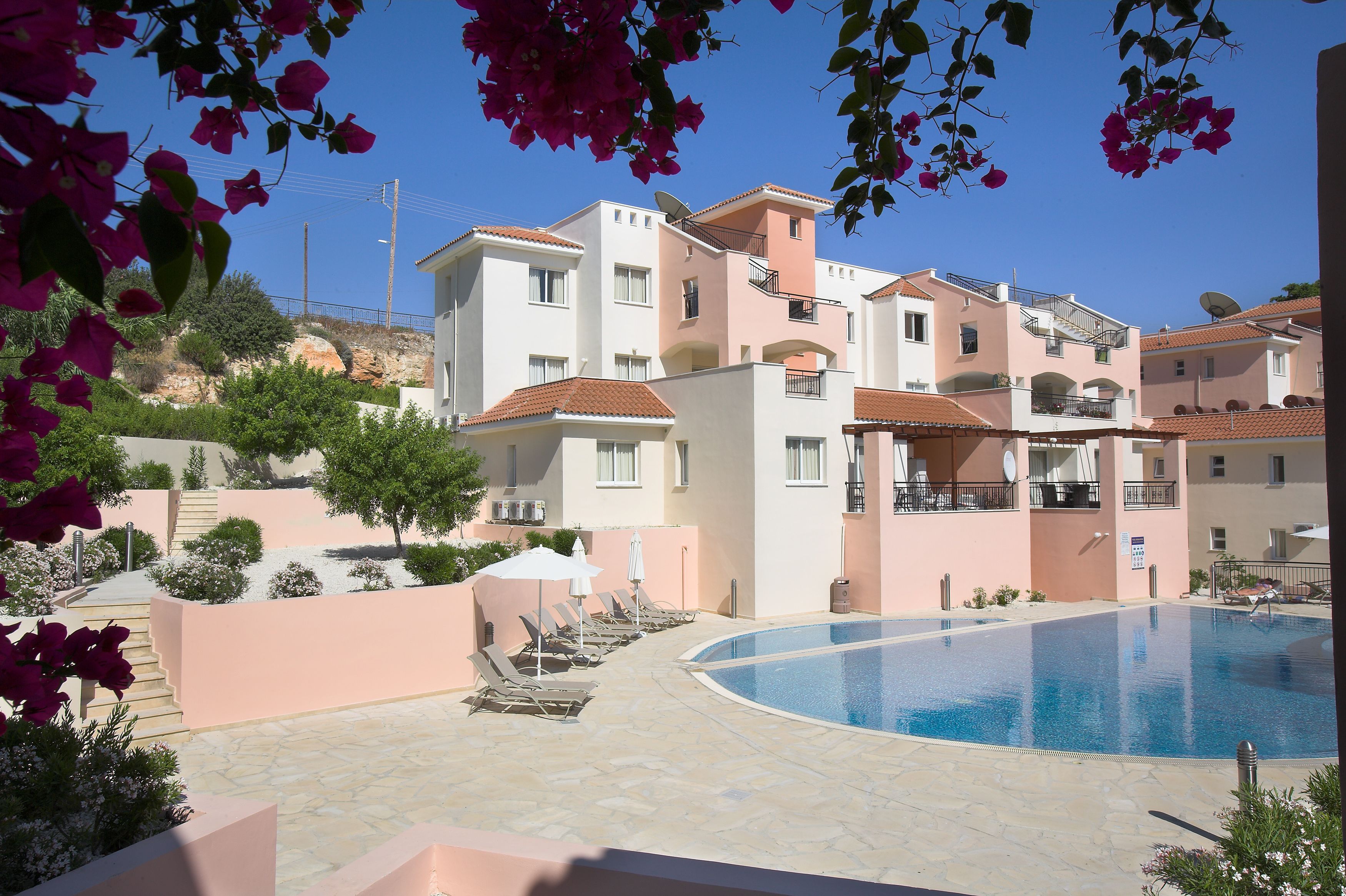 A pool area with lounge chairs and a clear blue pool, surrounded by buildings with balconies and satellite dishes.