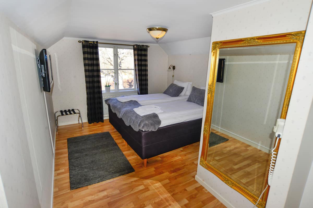 Un dormitorio con cama, una ventana con cortinas, un radiador, un espejo y suelo de madera.