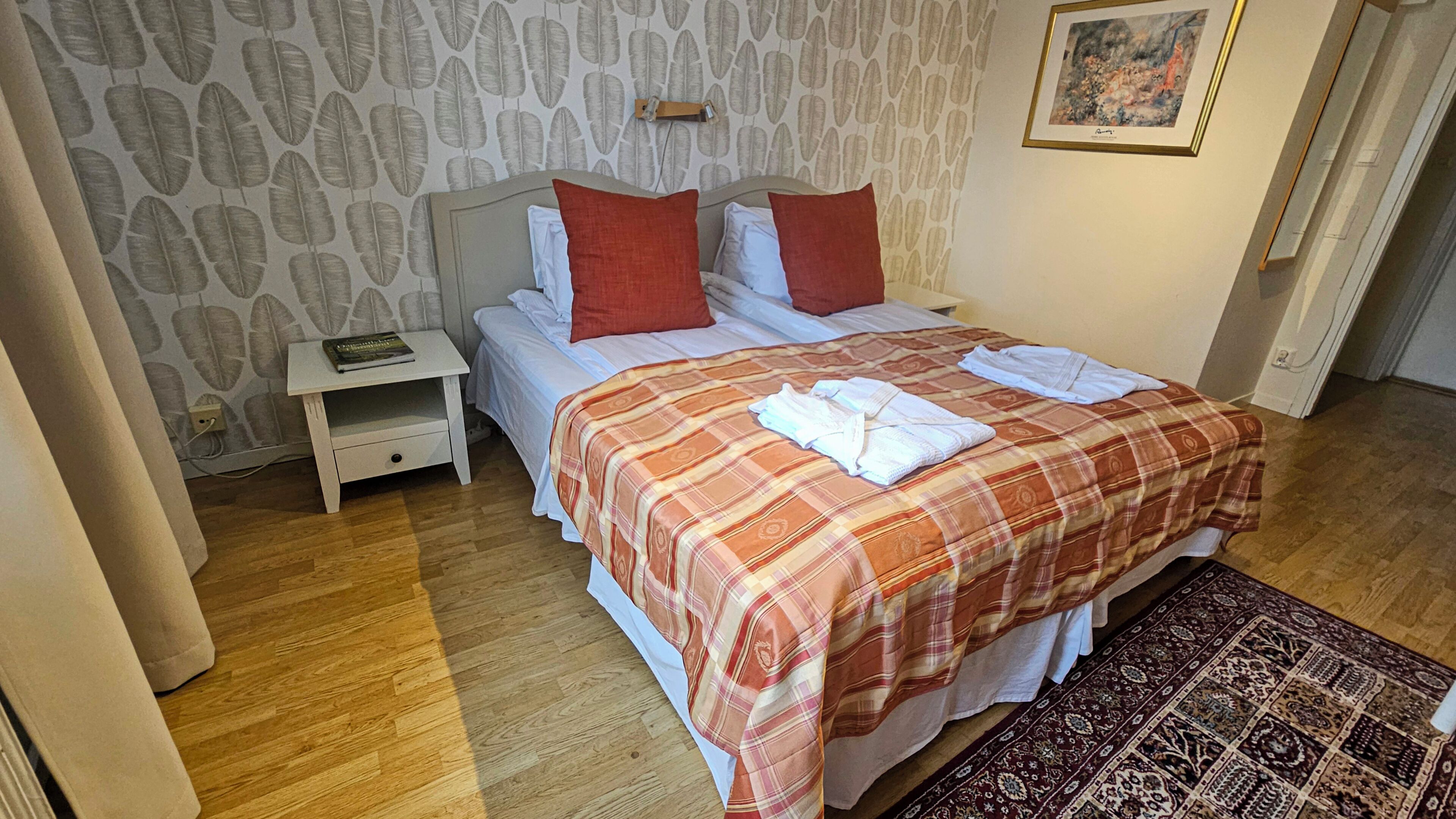 A neatly made bed with a plaid bedspread, a bedside table with a book, and a patterned wall.