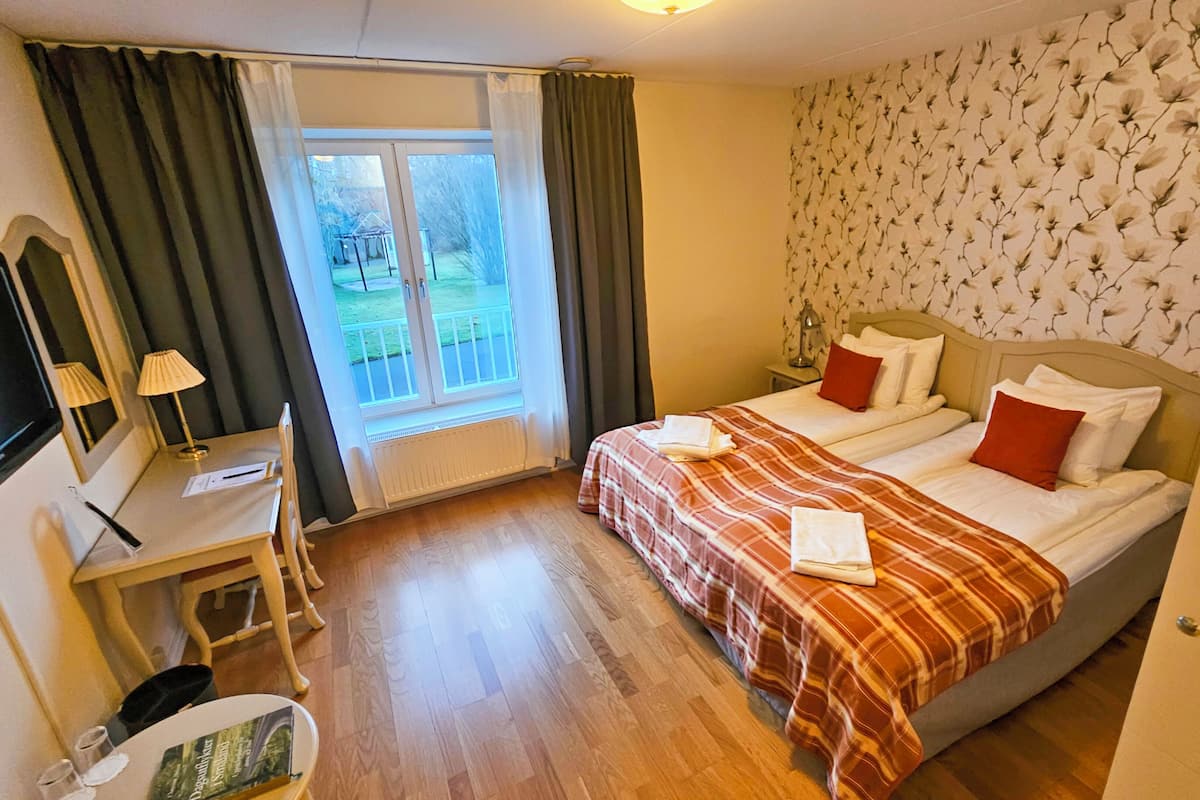 Una habitación de hotel con cama, escritorio con lámpara, televisión y ventana con cortinas.