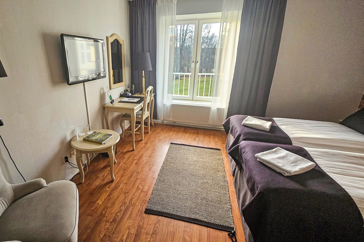 Habitación de hotel con cama, escritorio, silla, lámpara y vistas al exterior.