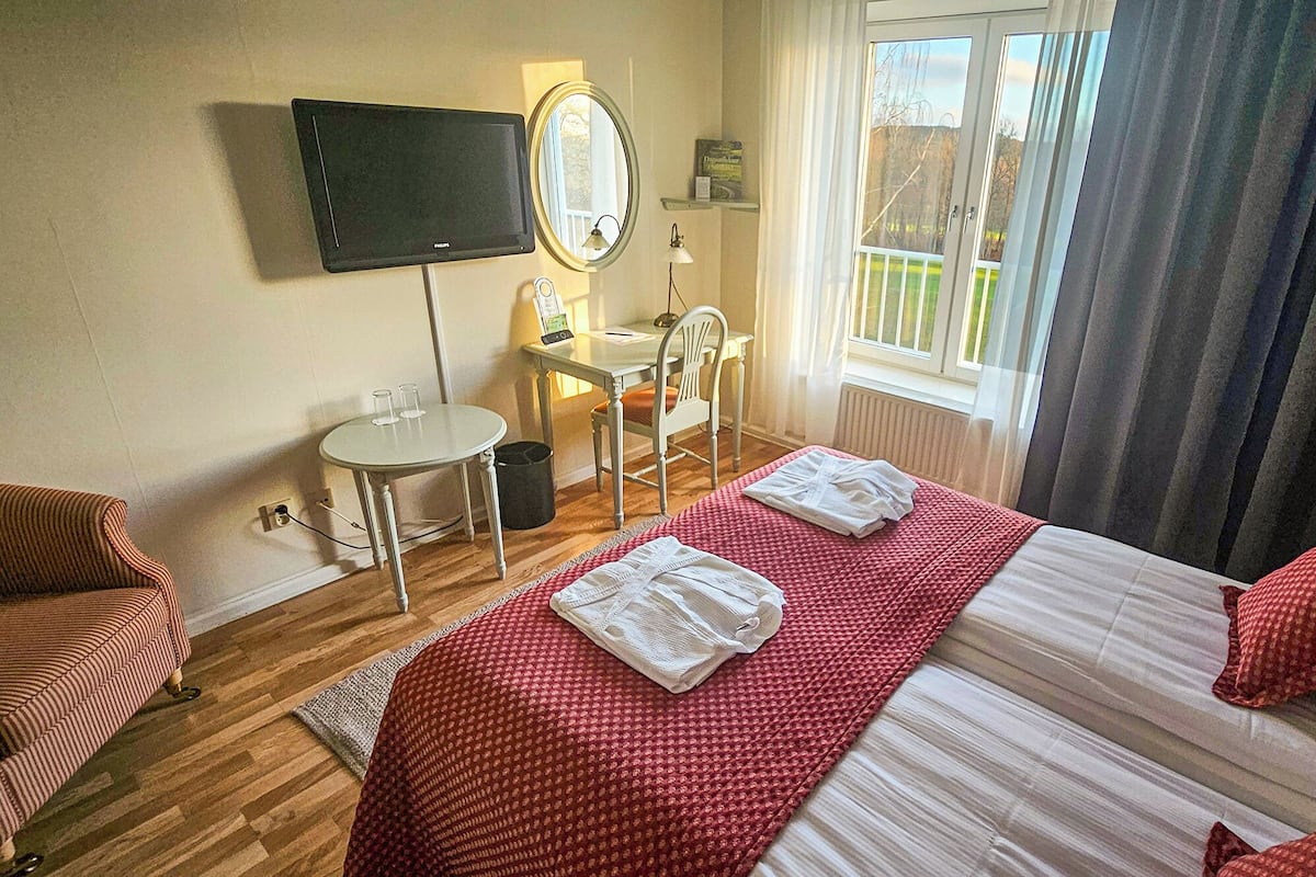 Habitación de hotel con cama, escritorio, silla, televisor y ventana con cortinas.