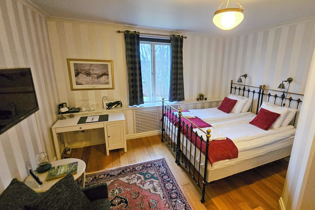 Un dormitorio con dos camas, un escritorio, una silla, un televisor y una ventana con cortinas.