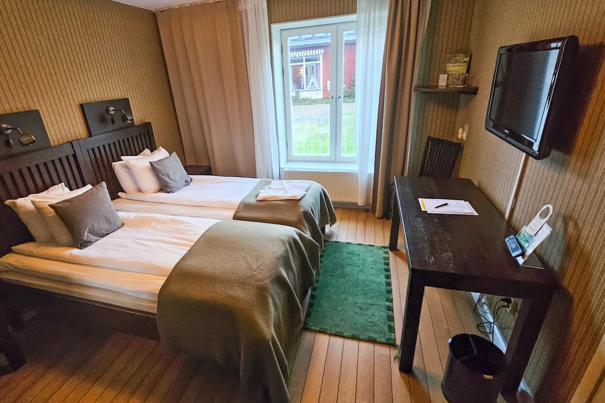 Habitación de hotel con dos camas, un escritorio, un televisor y vistas al exterior.