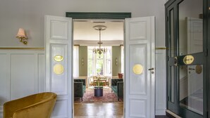 Un pasillo con piso a cuadros, una silla amarilla y un comedor con candelabro.