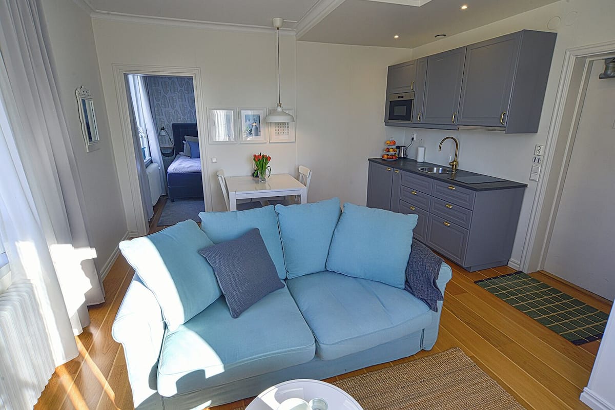 Una sala moderna con un sofá azul claro, una mesa de comedor y una cocina con armarios grises y un fregadero.