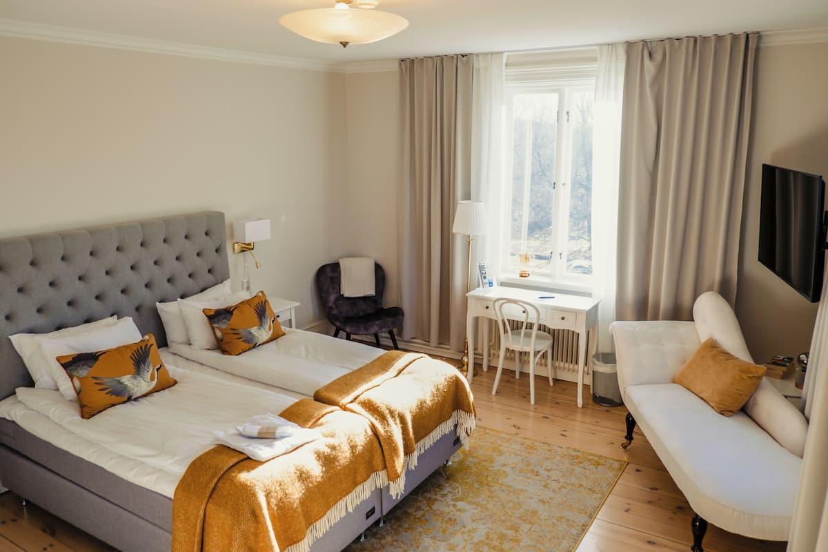 Habitación de hotel con cama, dos mesitas de noche, escritorio, silla, sofá, televisor y ventana con cortinas.