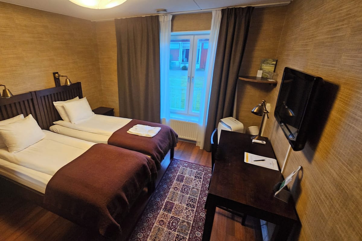 Habitación de hotel con dos camas, un escritorio, un televisor y una ventana con cortinas.