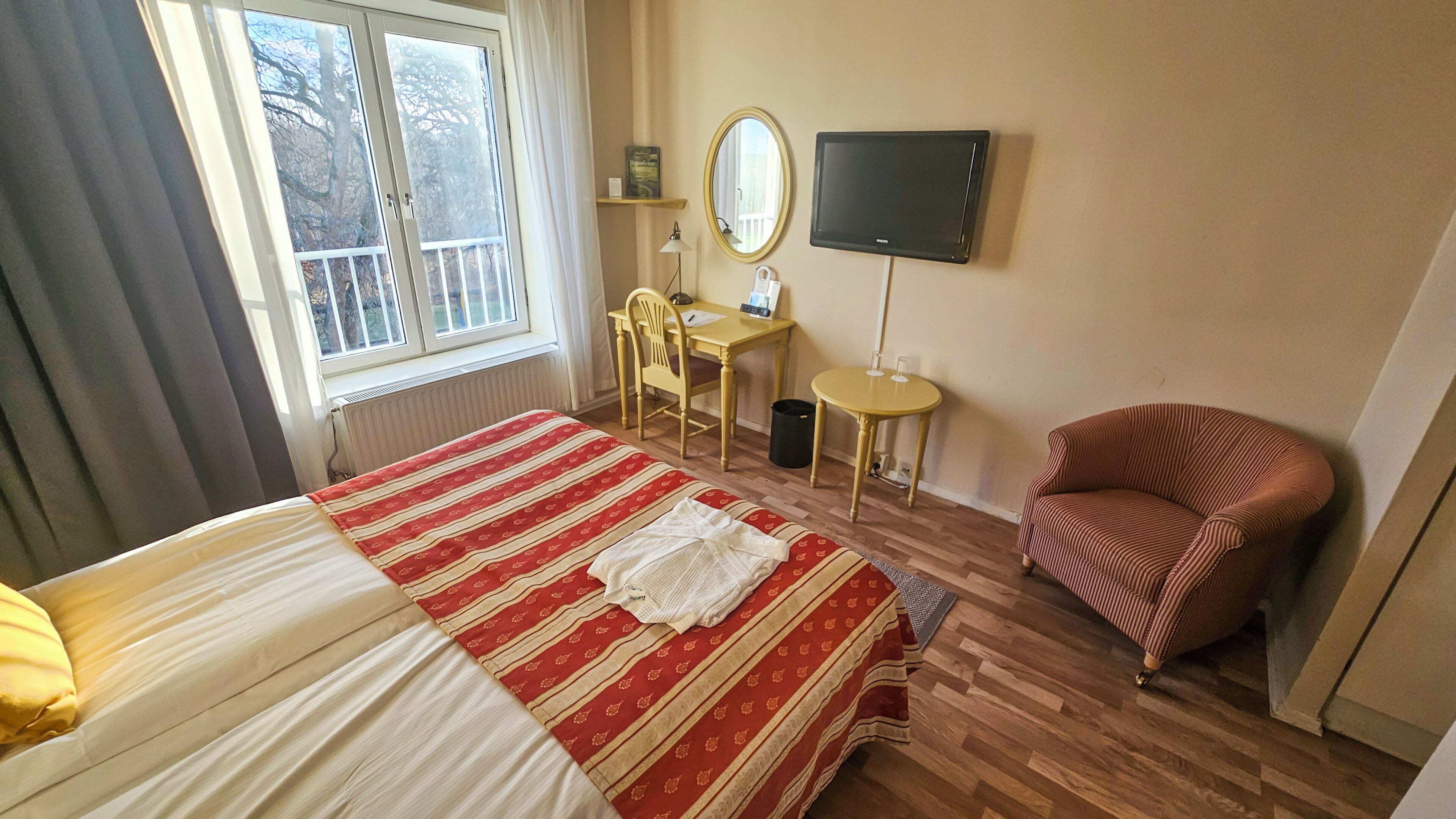 Una habitación de hotel con una cama, una silla, un escritorio, un televisor y una ventana.