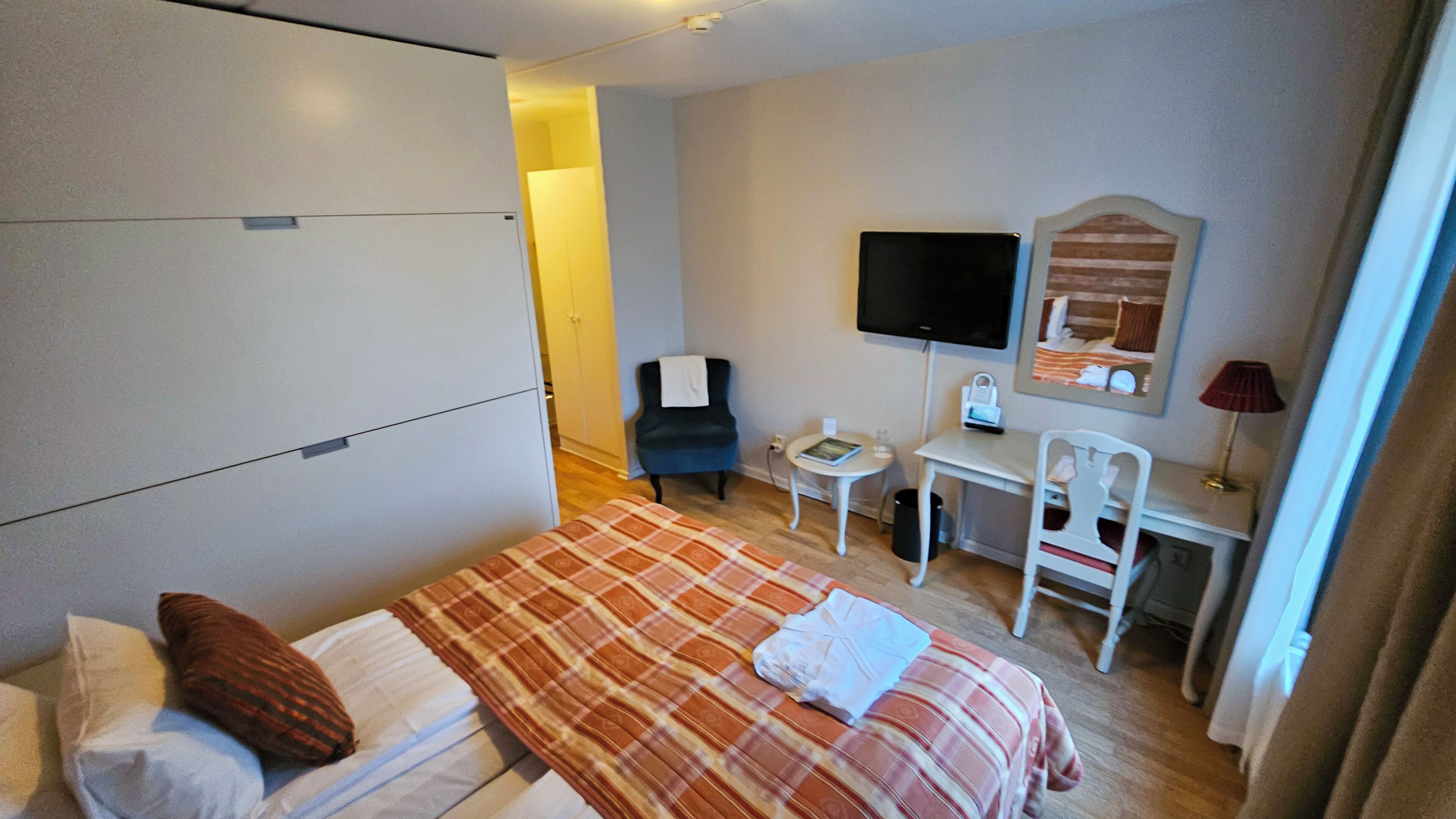 A hotel room with a bed, a desk, a chair, a TV, and a mirror.