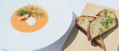 A white plate with a soup and a piece of toasted bread on a wooden board.
