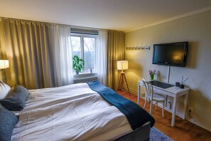 A hotel room with a bed, a desk, a chair, a television, and a window with curtains. - Fredensborgs Herrgård (Vimmerby)
