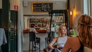 Una zona de bar con barra, estantes llenos de botellas y una persona sentada en una mesa.